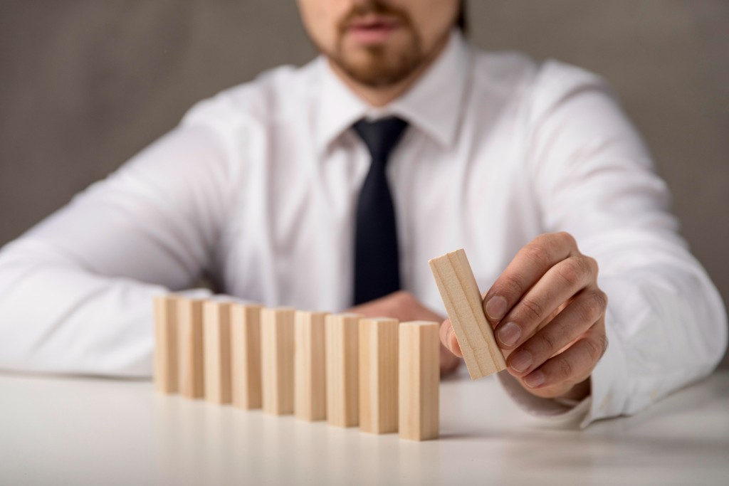 Leader in business dress carefully placing a wooden block in a row of blocks on a table—strategic, methodical building